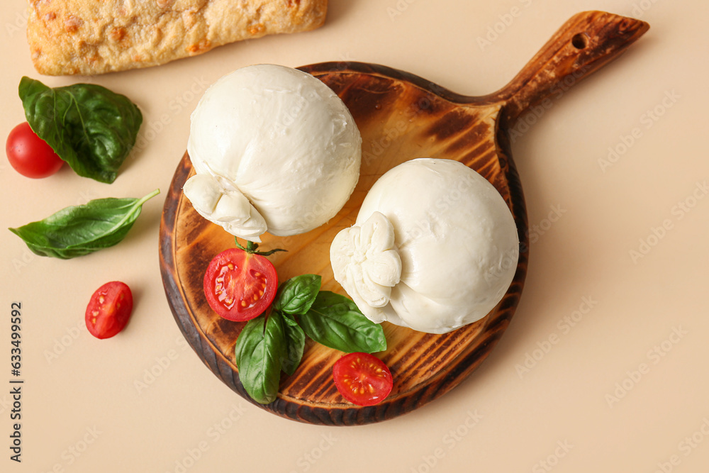 Wooden board of tasty Burrata cheese with basil and tomatoes on beige background