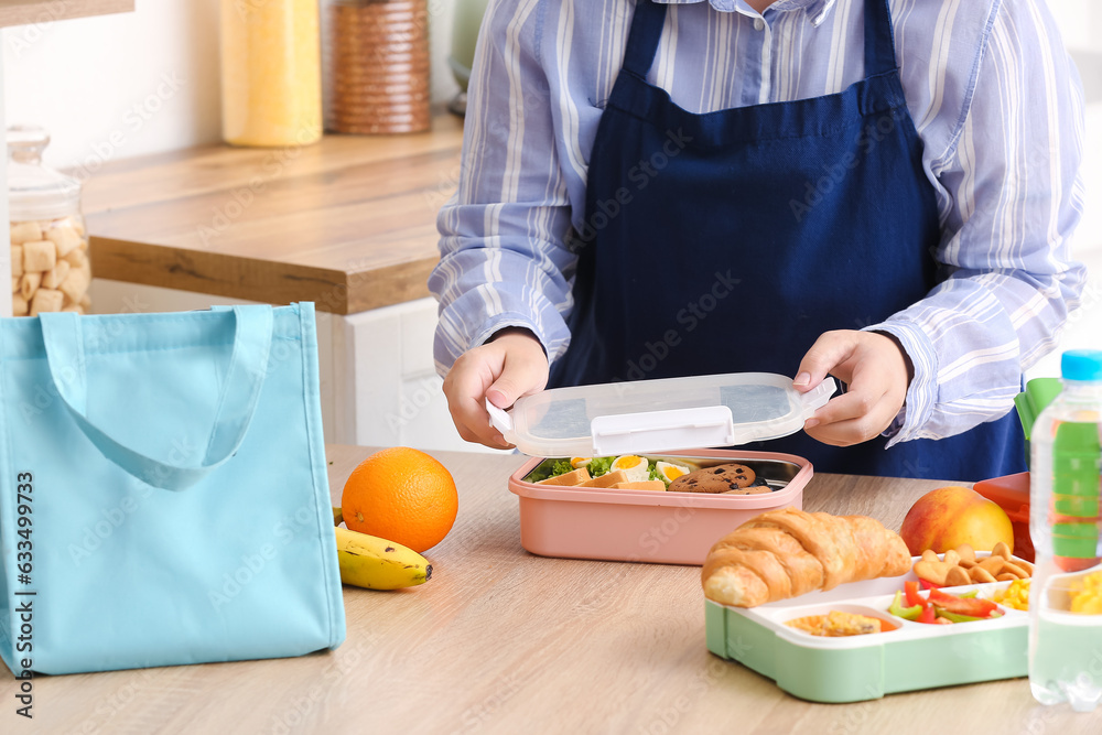 Mother packing meal in lunchbox for school on table at kitchen