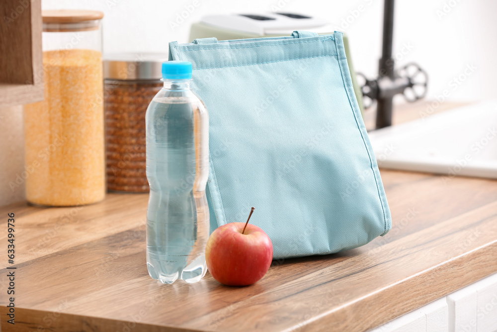 Lunch box bag with apple and bottle of water on table in kitchen