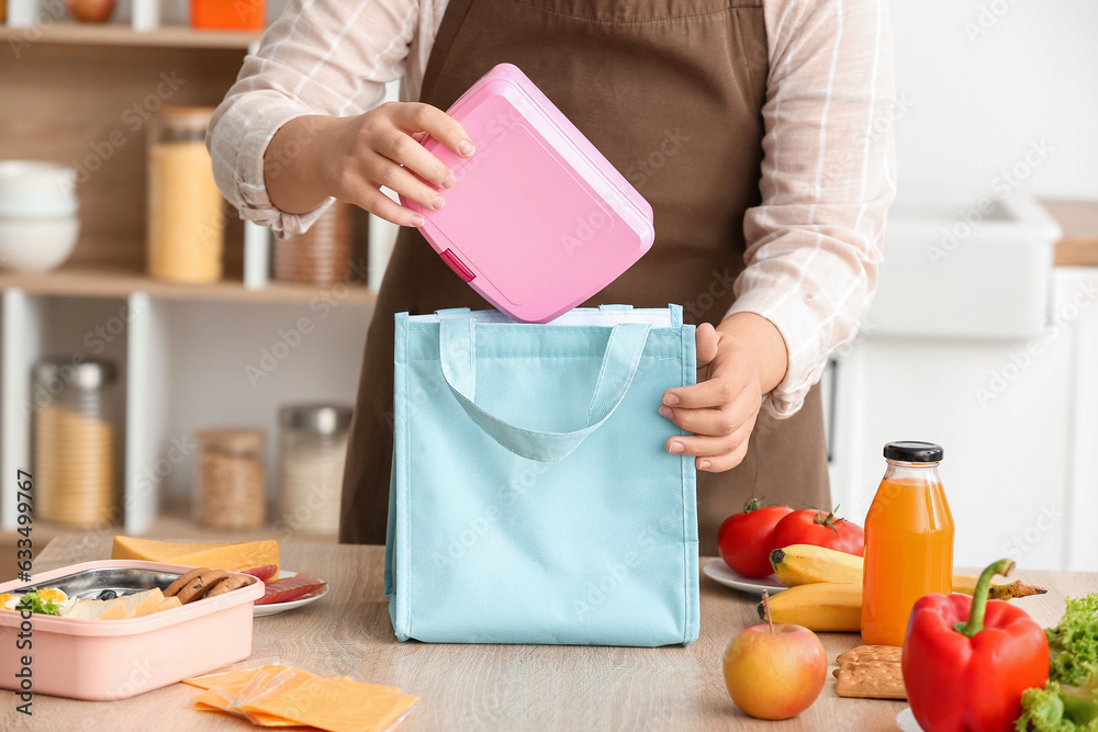 Mother packing meal for school lunch on table in kitchen