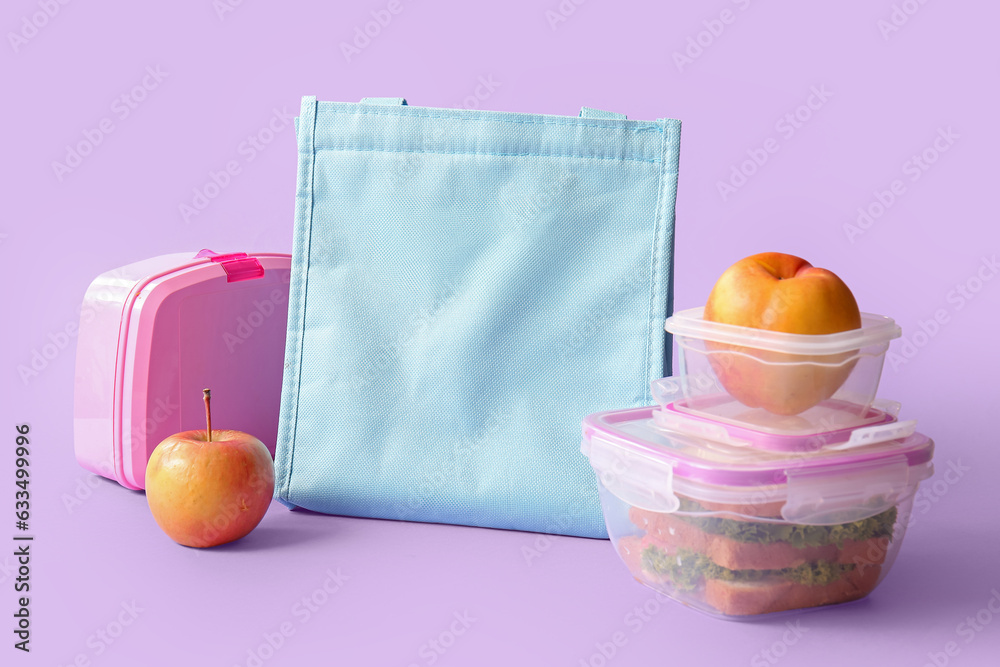 Bag, lunchboxes with delicious food and fruits on lilac background