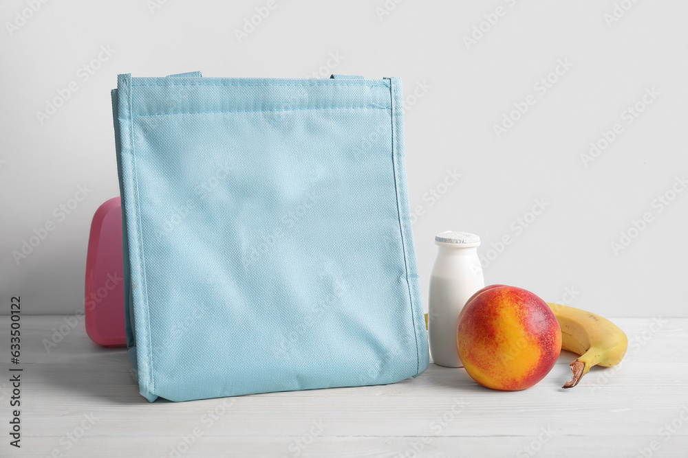 Bag, lunchbox with delicious food and fruits on white wooden table near wall