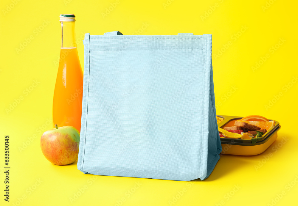 Bag, lunchbox with delicious food and bottle of juice on yellow background