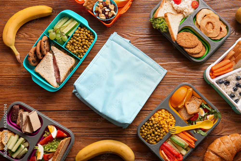 Bag, lunchboxes with different delicious food and fruits on brown wooden background