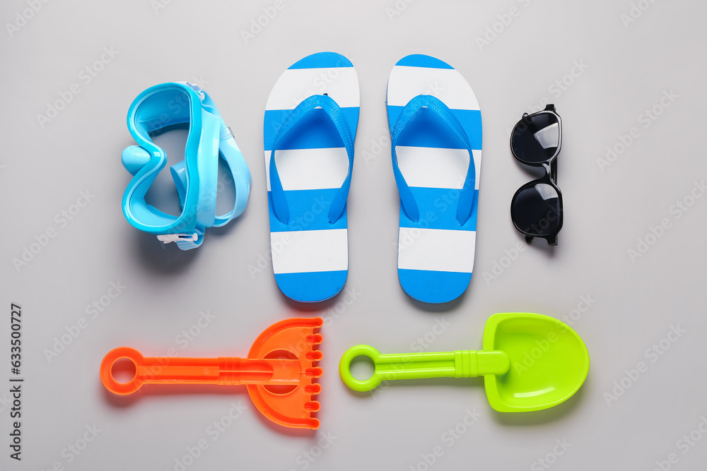 Female stylish flip flops with sunglasses, snorkeling mask and beach toys on grey background