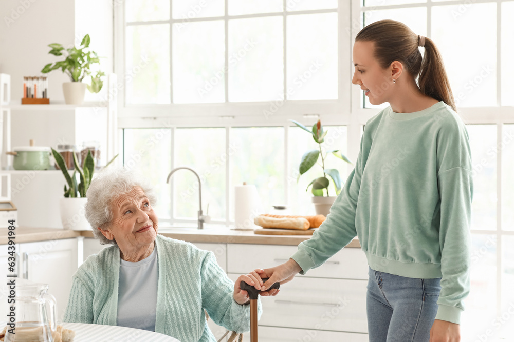 Senior woman with walking stick and her granddaughter in kitchen