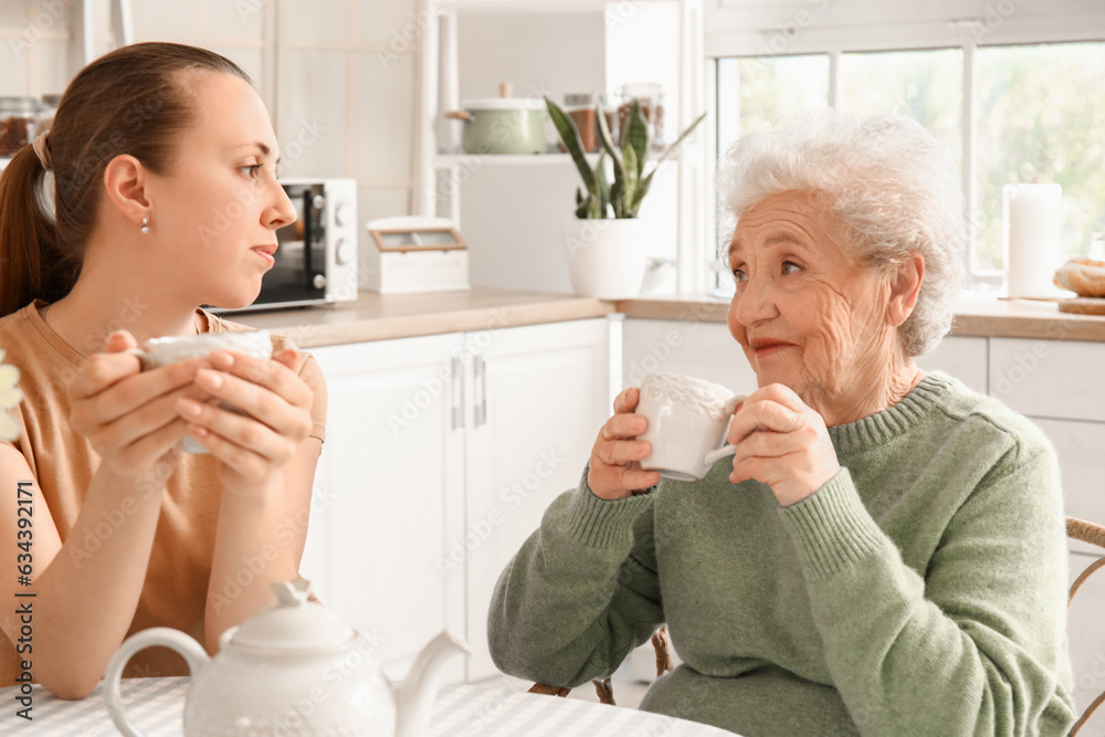 Senior woman with her granddaughter drinking tea in kitchen