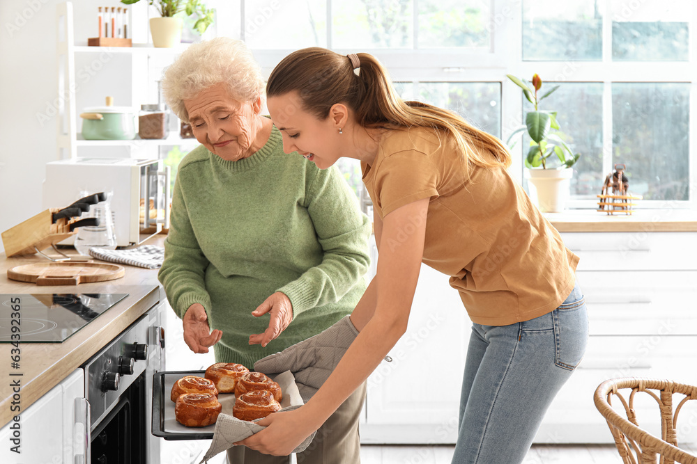 Senior woman with her granddaughter taking buns from oven in kitchen