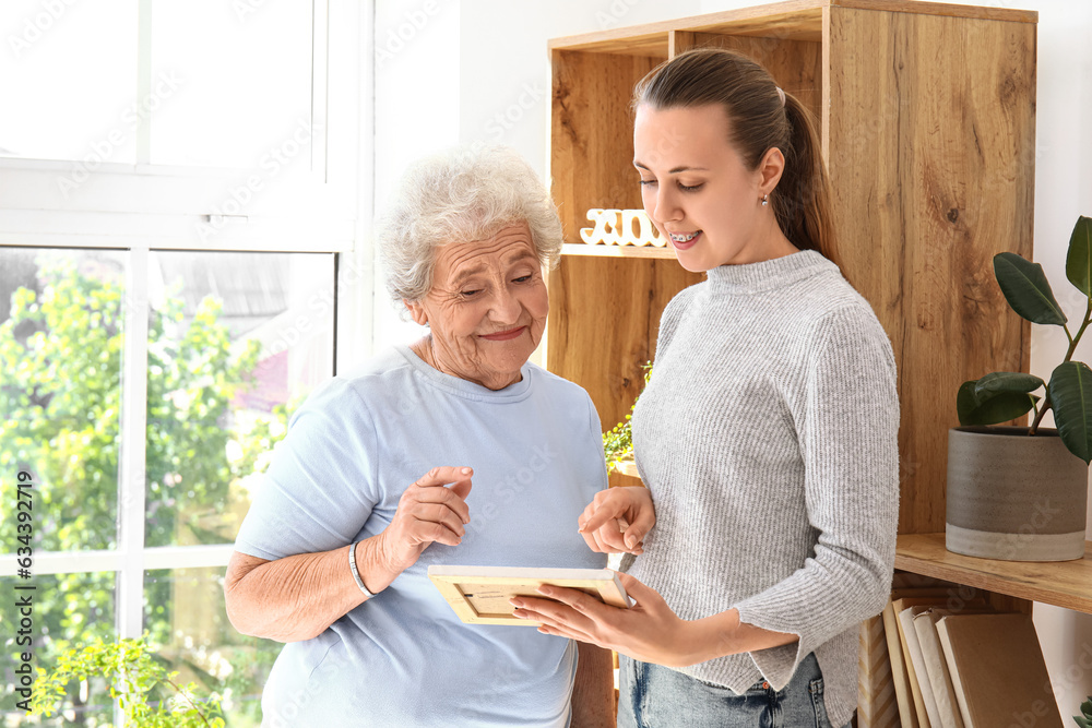 Senior woman with her granddaughter and photo frame at home