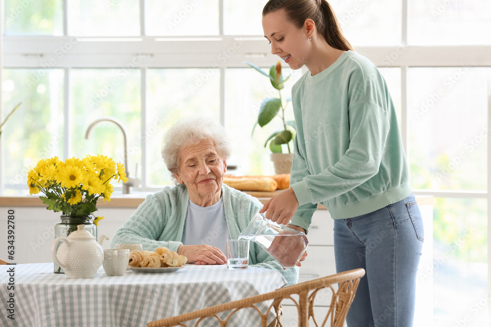 Young woman pouring water into glass for her grandmother in kitchen