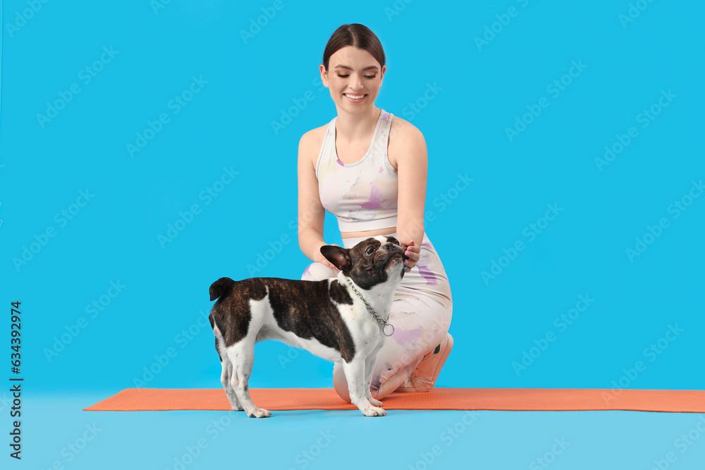 Sporty young woman with her French bulldog on blue background