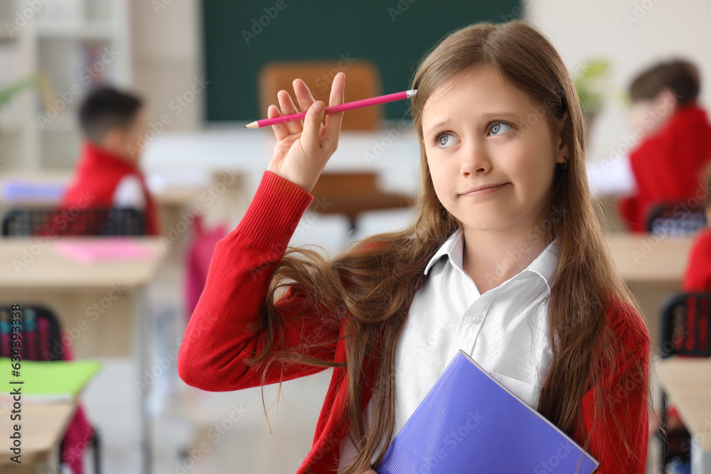 Thoughtful little schoolgirl with copybook in classroom