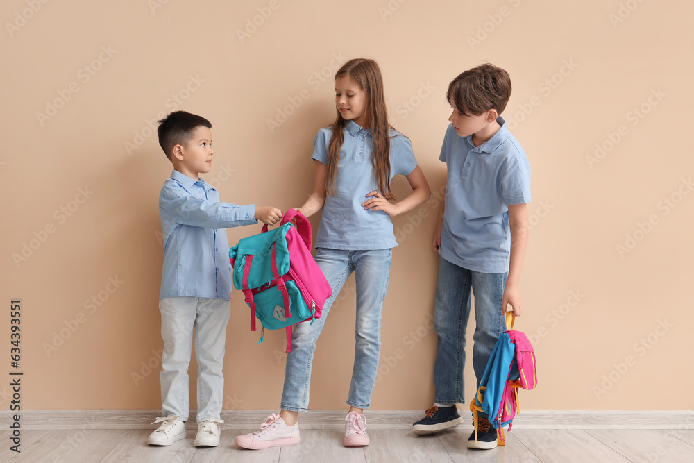 Little pupils with backpacks near beige wall