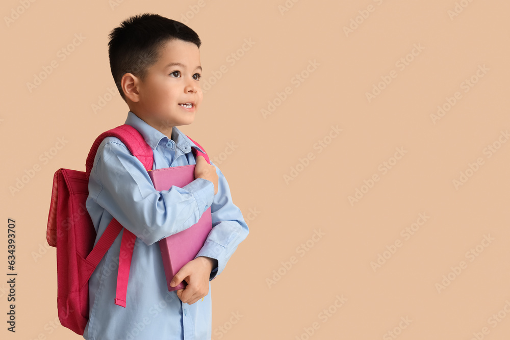 Little schoolboy with book on beige background