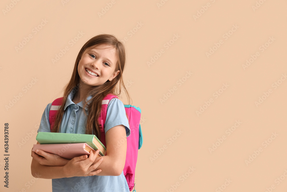 Little schoolgirl with books on beige background