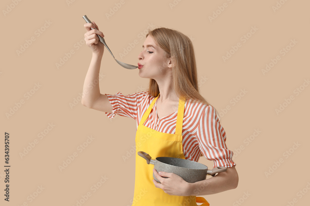 Young woman with ladle and cooking pot on beige background