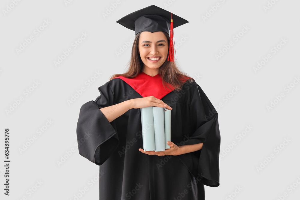 Female graduate student with books on light background