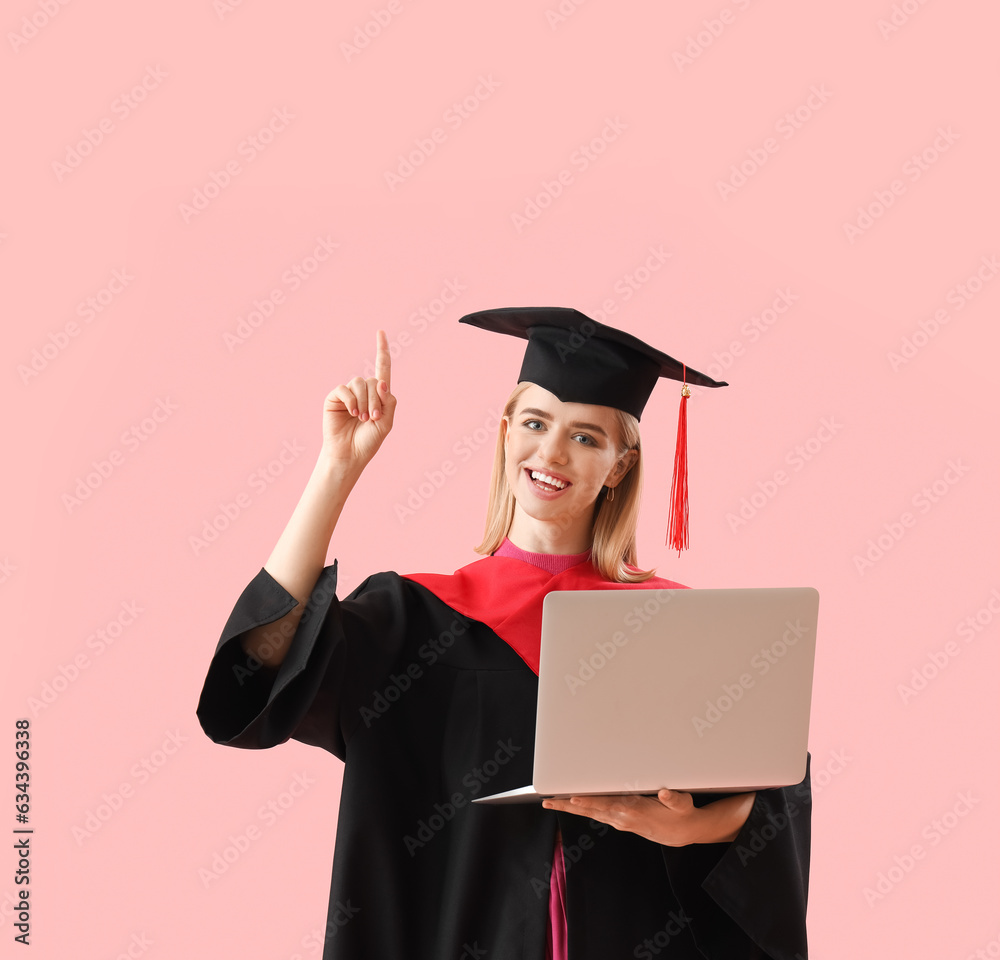 Female graduate student with laptop pointing at something on pink background