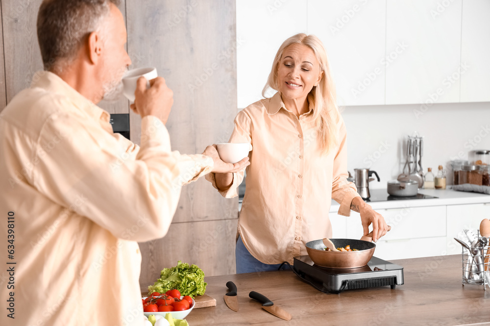 Mature man giving cup of coffee to his wife in kitchen