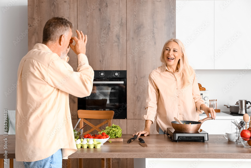 Mature woman with her funny husband cooking in kitchen