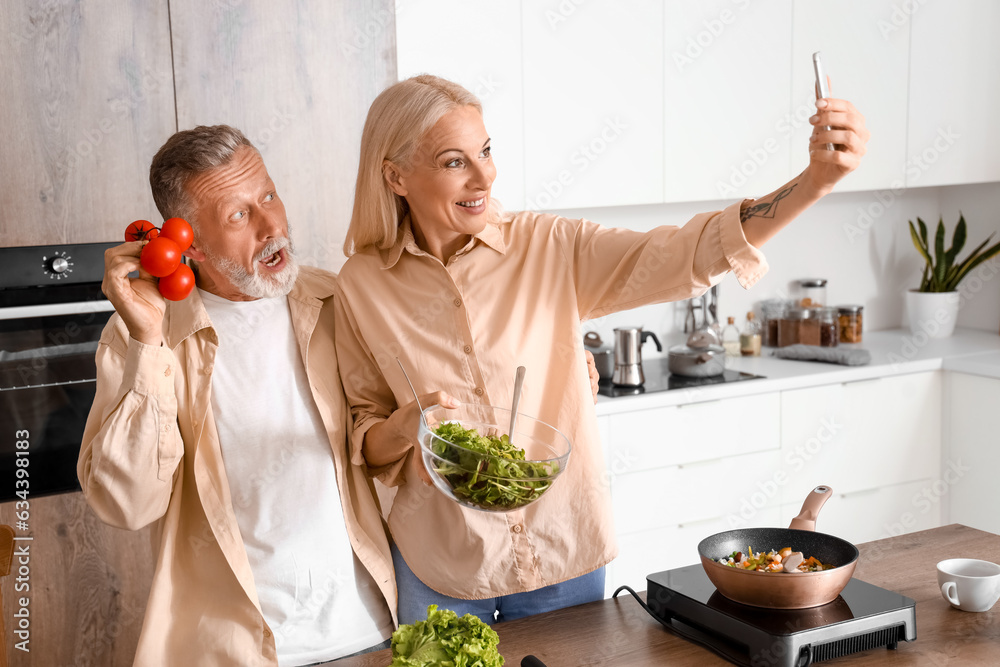 Mature couple with tomatoes taking selfie in kitchen