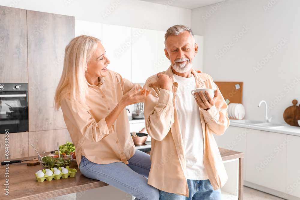 Mature man with cup of coffee and his wife in kitchen