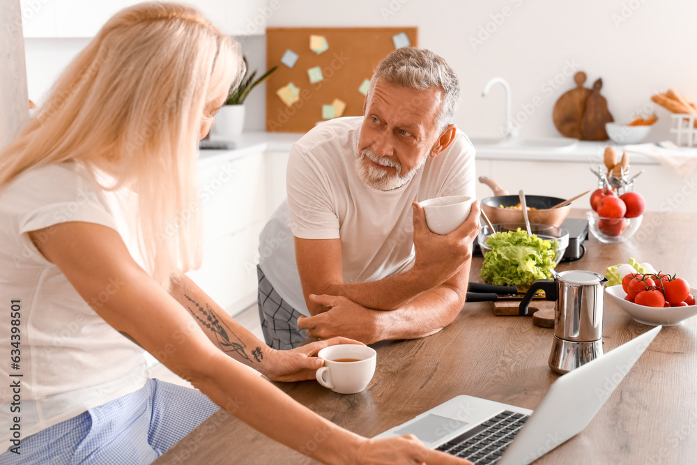 Mature couple with laptop drinking coffee in kitchen