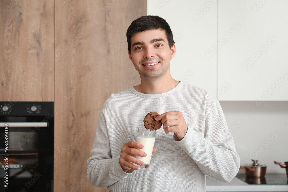 Young man with glass of milk and cookie in kitchen