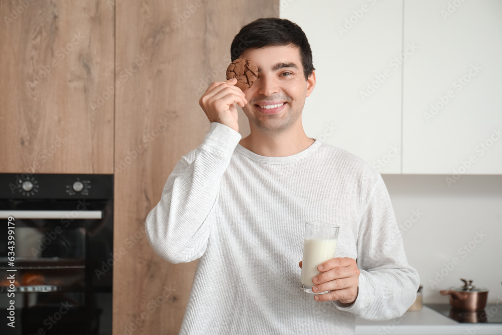 Young man with glass of milk and cookie in kitchen