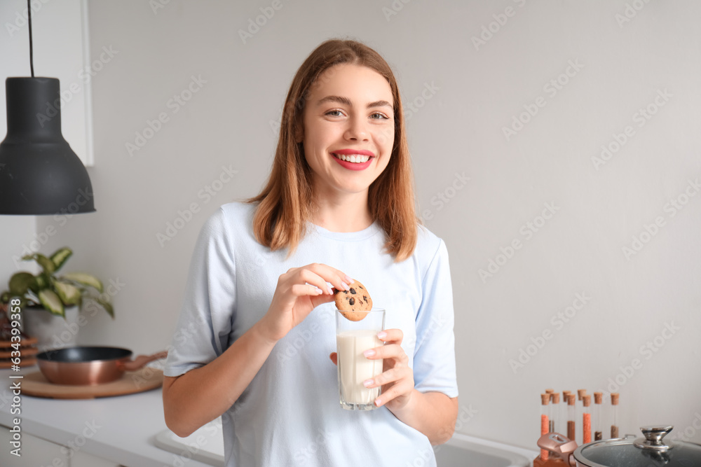 Young woman with glass of milk and cookie in kitchen