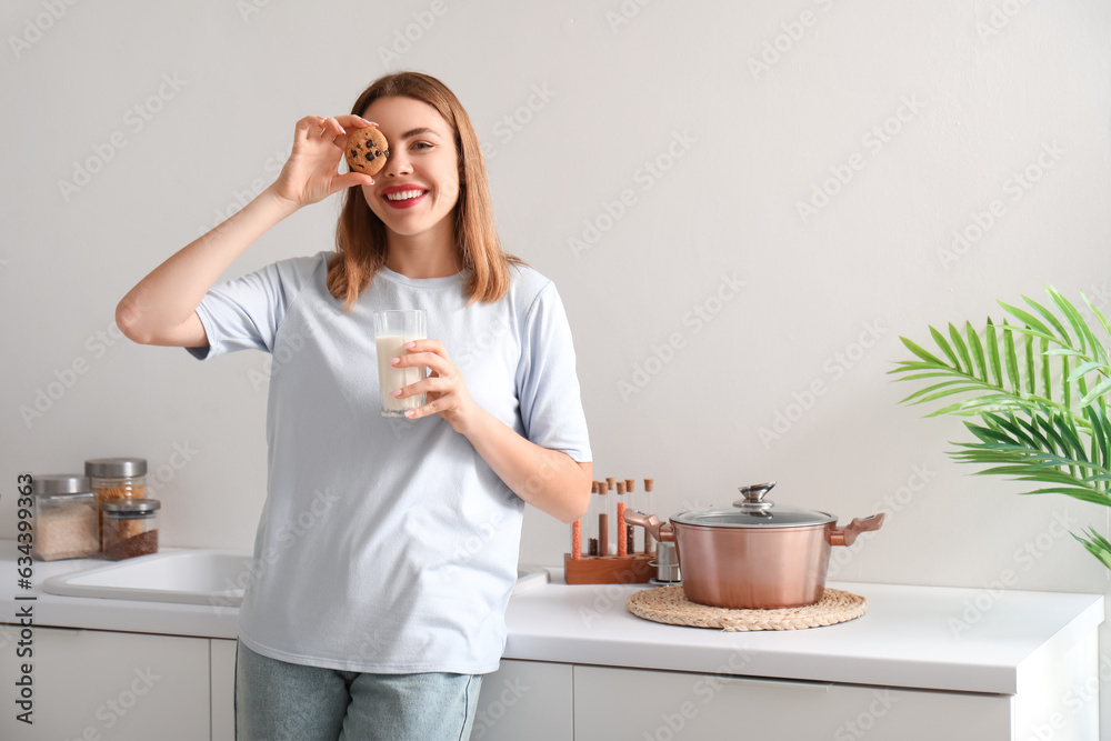 Young woman with glass of milk and cookie in kitchen