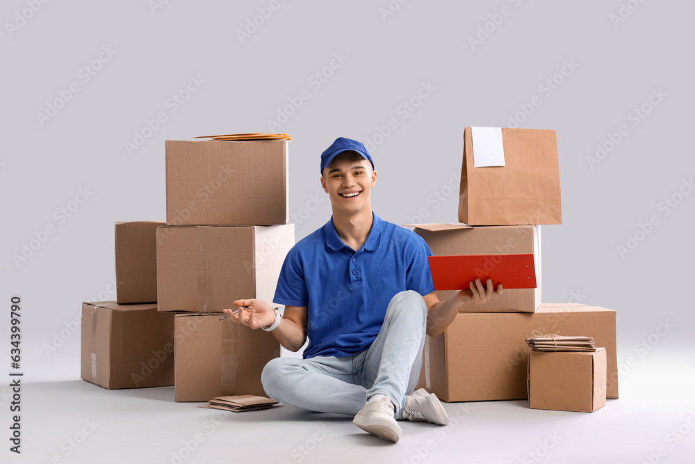 Young courier with clipboard and parcels on light background