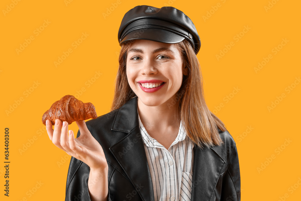 Beautiful young woman with tasty croissant on yellow background