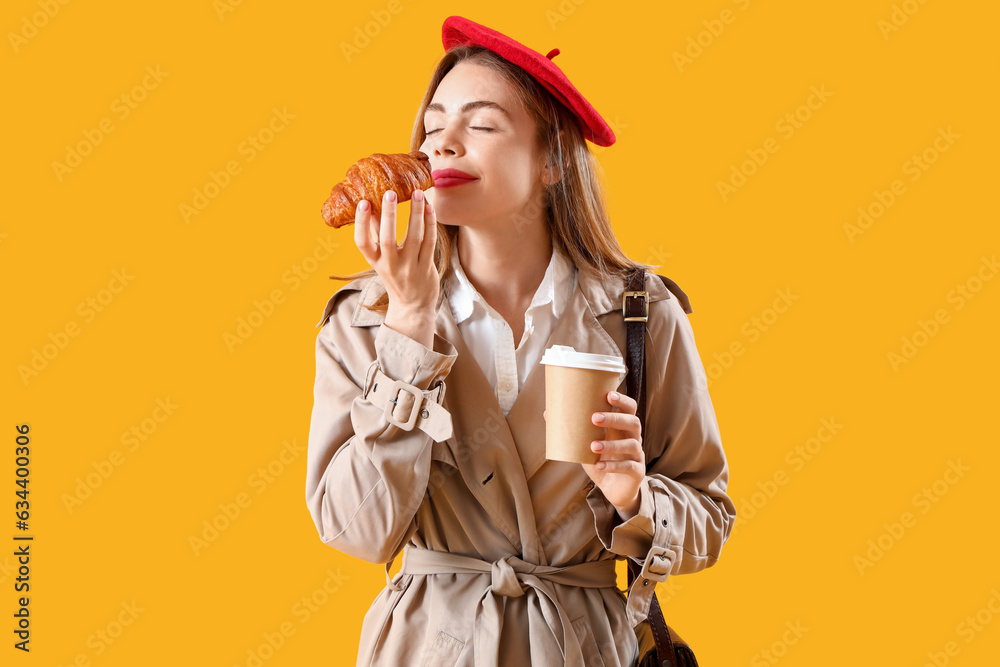 Beautiful stylish young woman in beret with tasty croissant and cup of coffee on yellow background