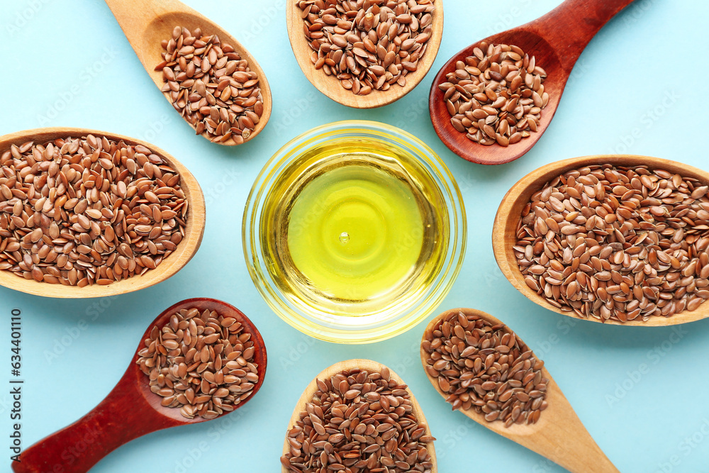 Glass bowl of flax oil and wooden spoons with seeds on blue background