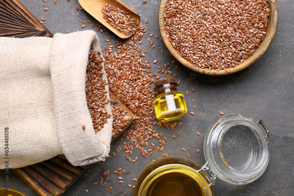 Jars of flax oil and wooden bowl with seeds on grey background