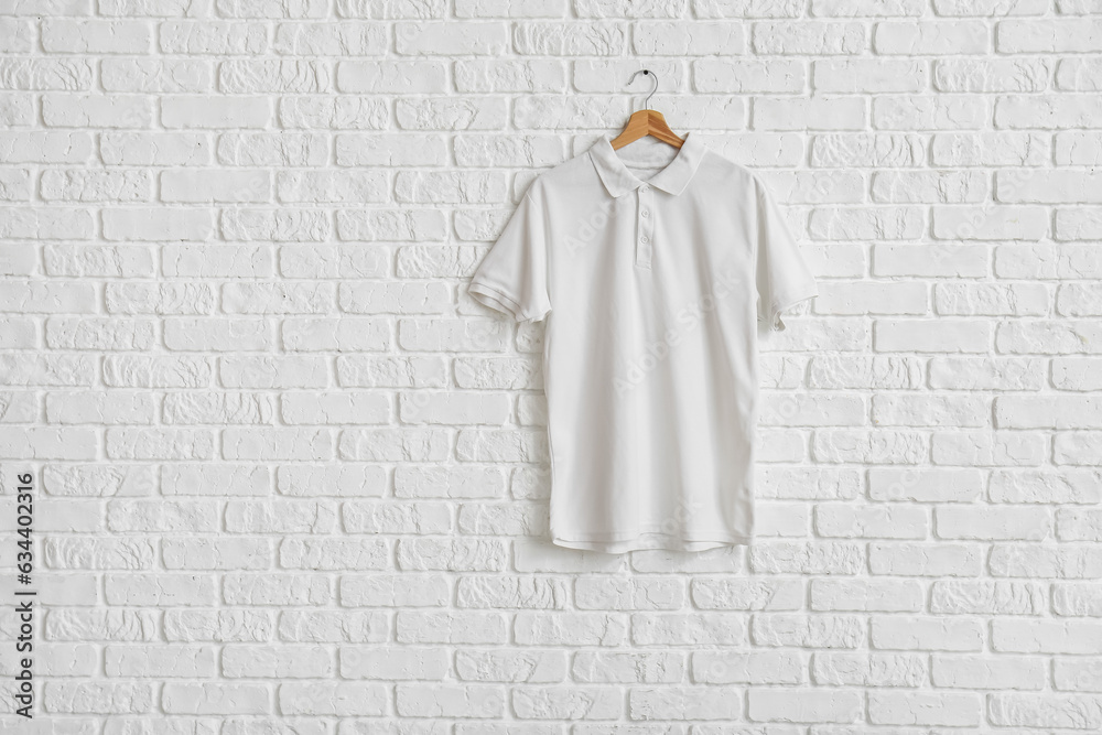 Stylish t-shirt hanging on white brick wall