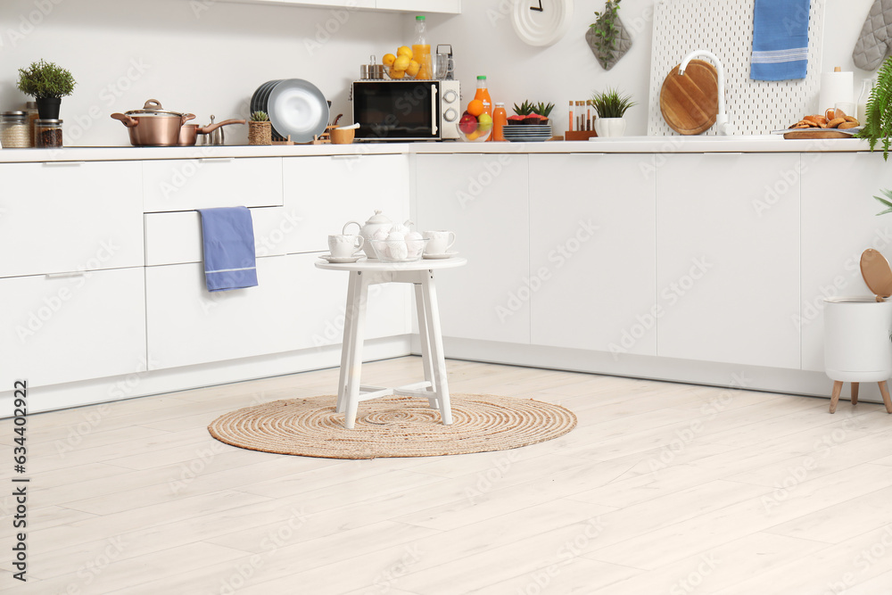 Small table with tea set and zephyr on wicker rug in modern kitchen