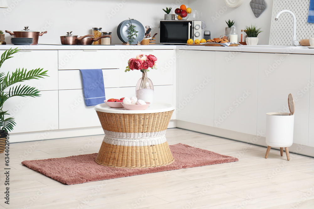 Coffee table with peony flowers and sweets on soft rug in modern kitchen