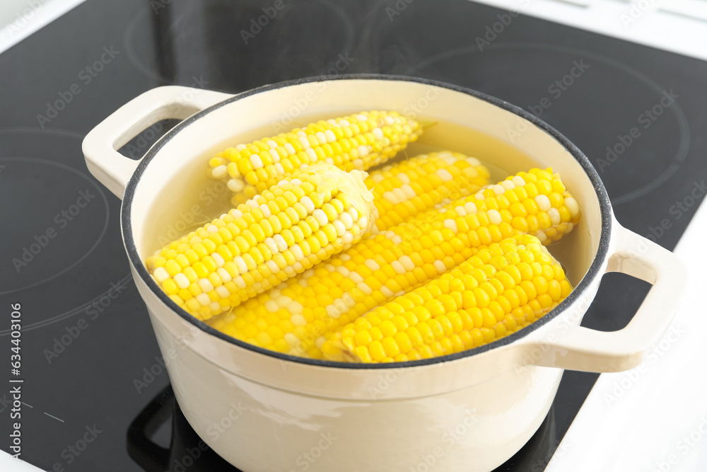 Cooking pot with boiling corn cobs on electric stove in kitchen