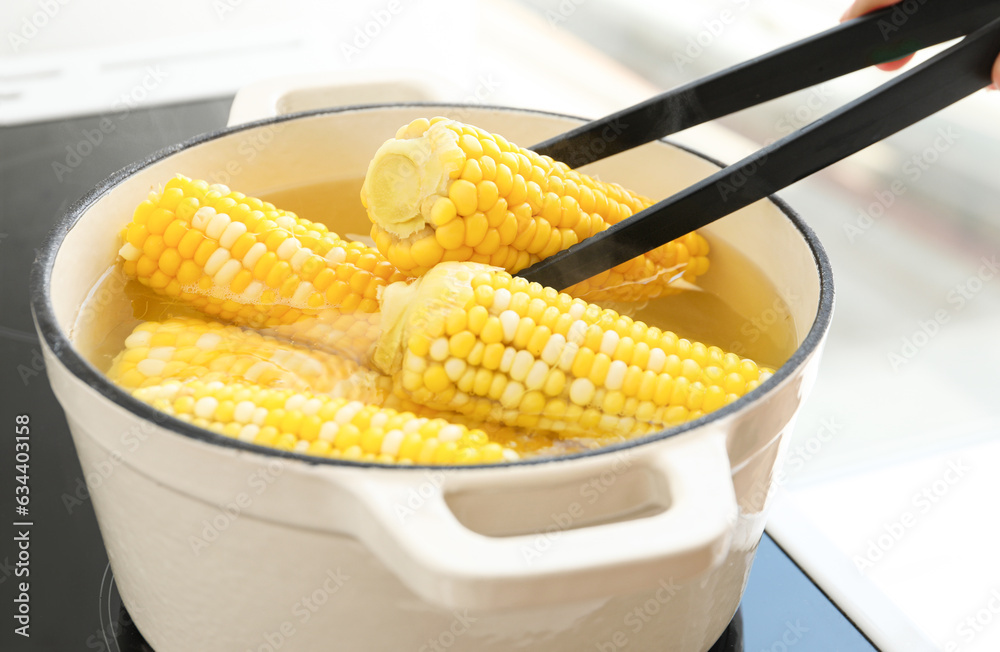 Cooking pot with boiling corn cobs on electric stove in kitchen