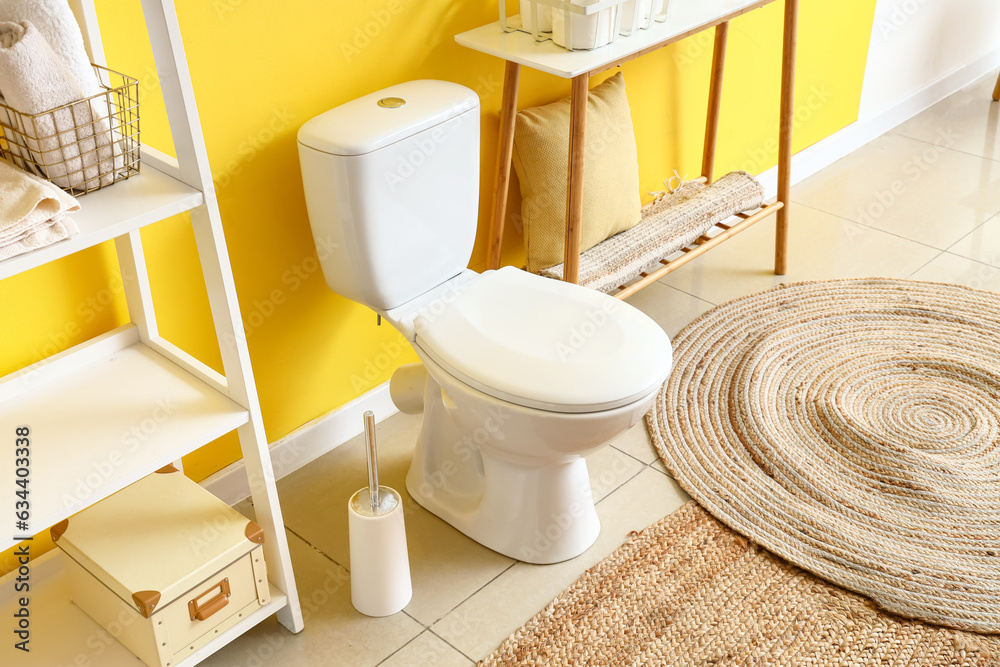 Interior of modern restroom with ceramic toilet bowl and paper holder near yellow wall