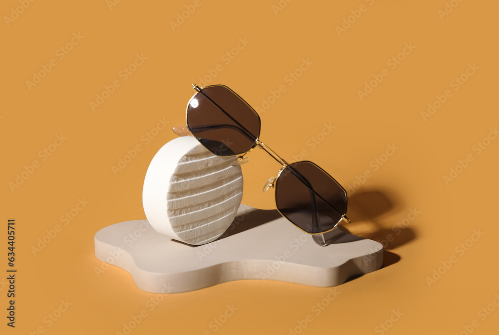 Stands with stylish retro sunglasses on orange background