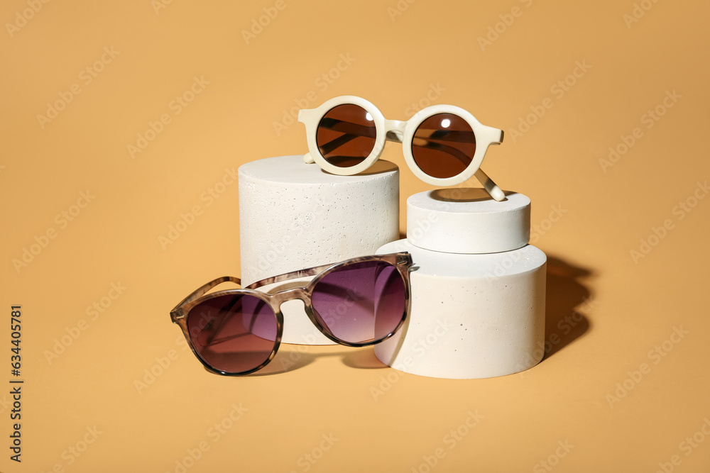 Stands with different stylish sunglasses on orange background