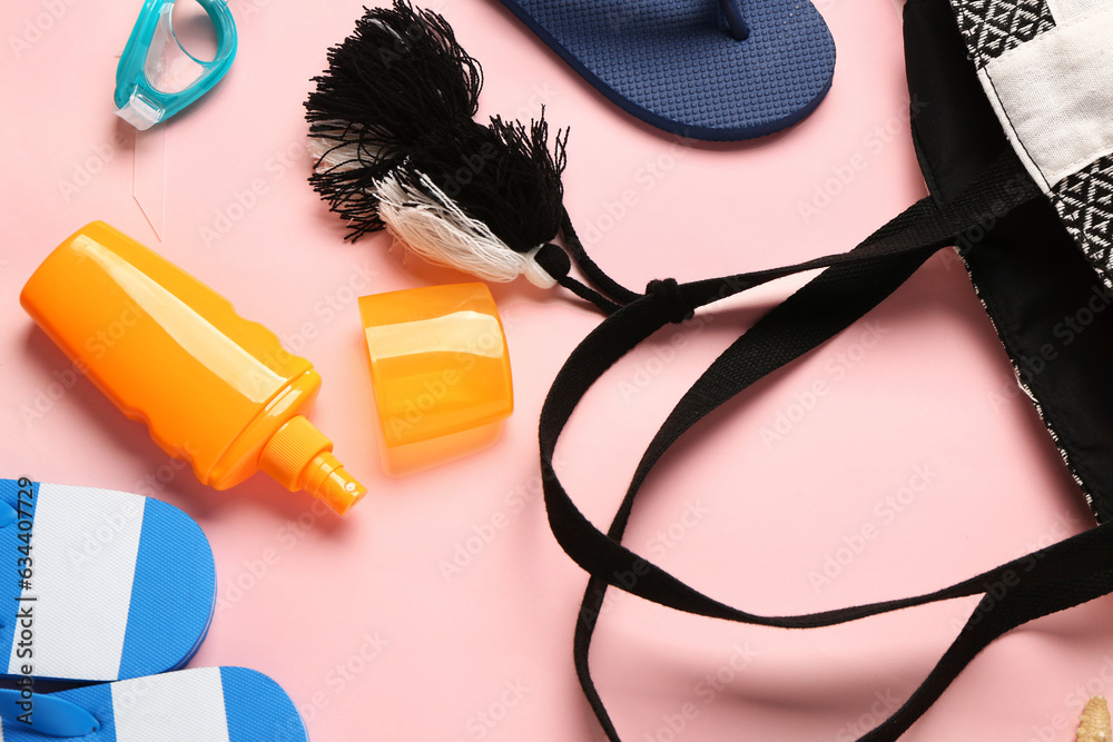 Bottle of sunscreen cream with bag and flip flops on pink background