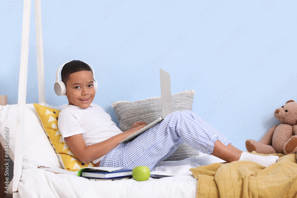 Little African-American boy with laptop studying computer sciences online in bedroom