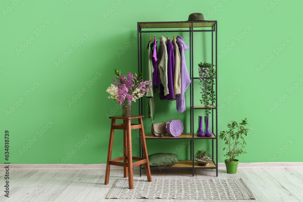 Interior of stylish room with shelving unit, clothes and stool