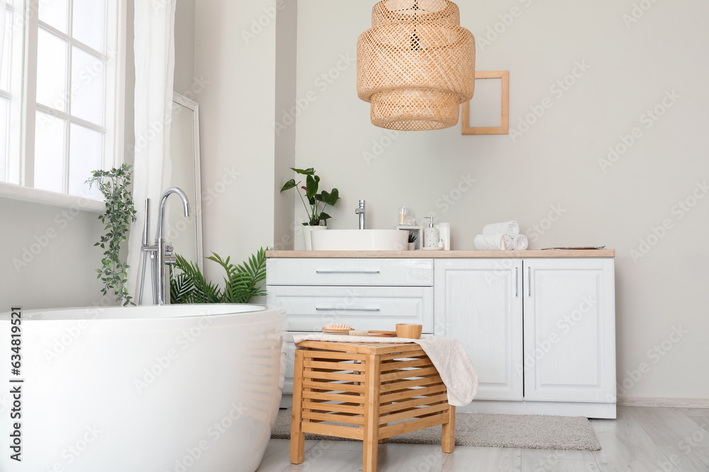 Interior of light bathroom with sink bowl on white counters, mirror and bathtub