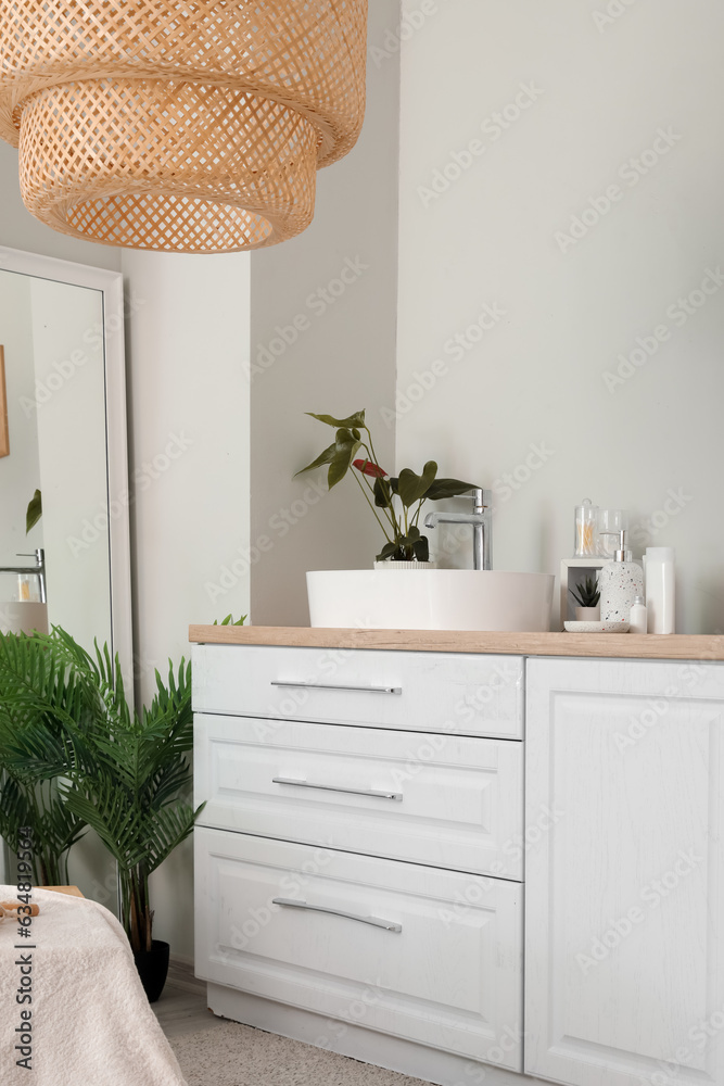 Interior of light bathroom with sink bowl on white counters and mirror