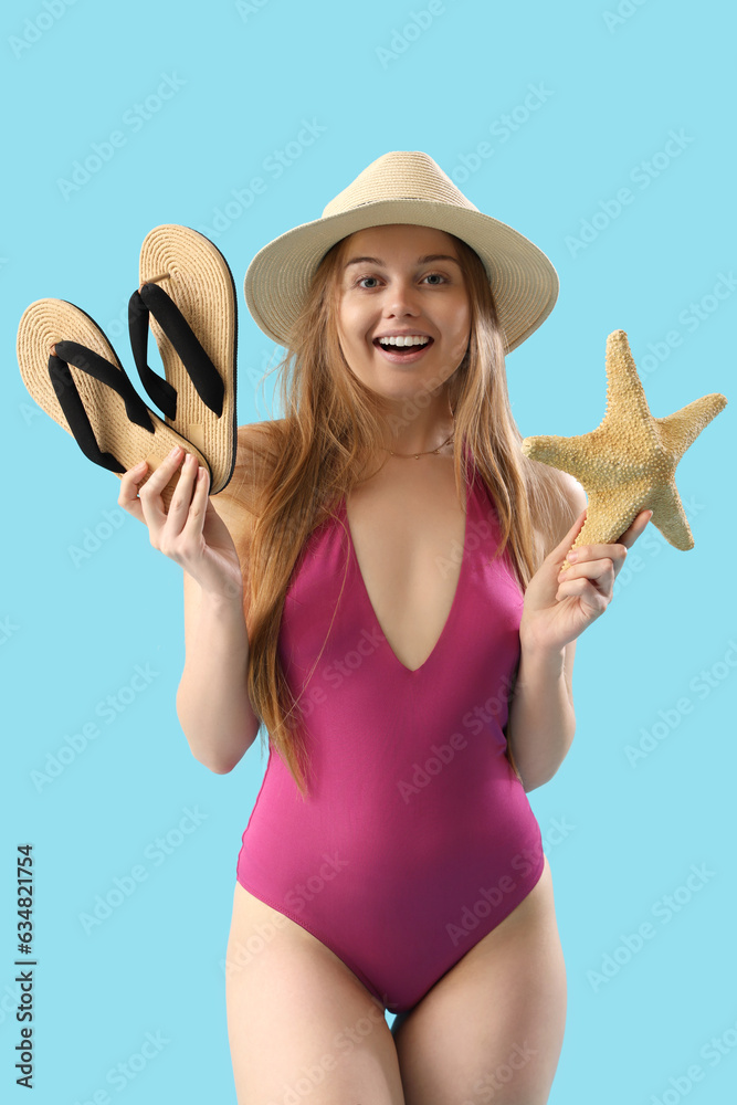 Beautiful young woman with flip-flops and starfish on blue background